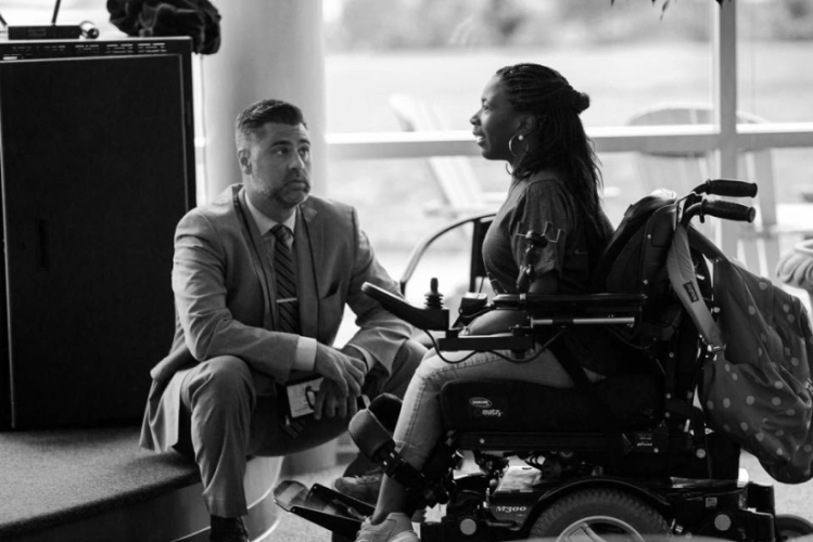 Man kneeling in front of a woman sitting in a wheelchair having a conversation. 