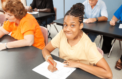 A black woman with braids working at a desk in a classroom.