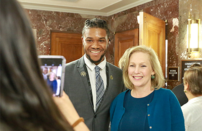 A young man in a suit having his photo taken with a congresswoman.