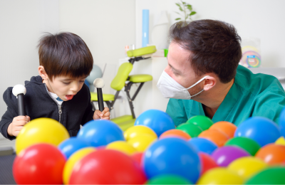 Image of a young boy and an adult medical personnel interacting next to a pile of colorful plastic balls.