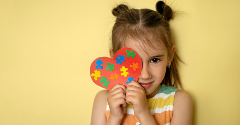 Image of a young child holding up a heart with puzzles pieces on it.
