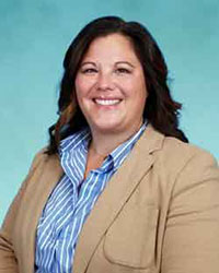 Woman with long brown hair wearing a tan suit and blue striped shirt