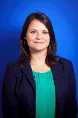 White woman with shoulder length brown hair wearing a blue blazer and green top