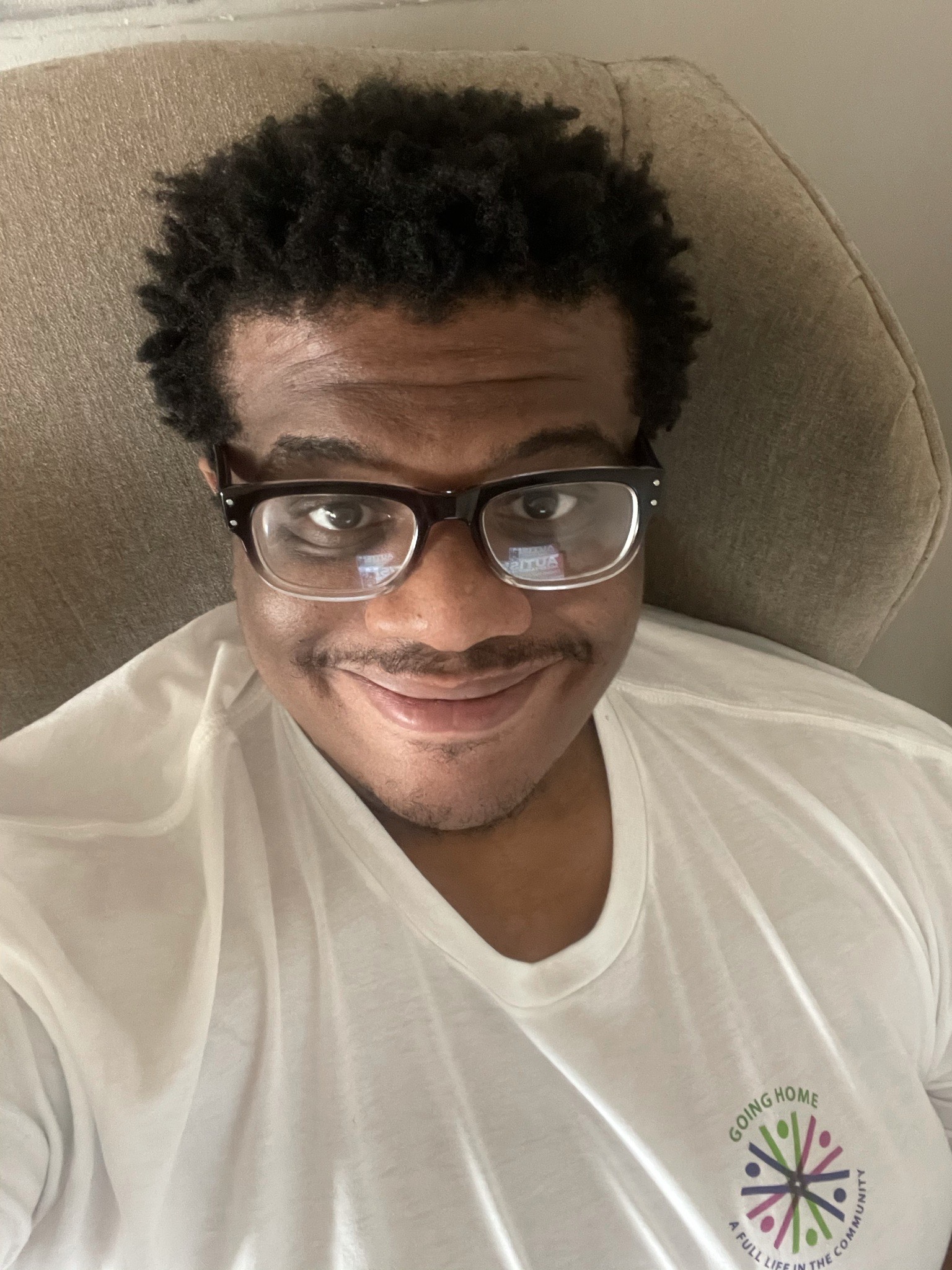 Image of Timotheus, a Black man with glasses wearing a tshirt with a logo that says Going Home, A Full Life in the Community