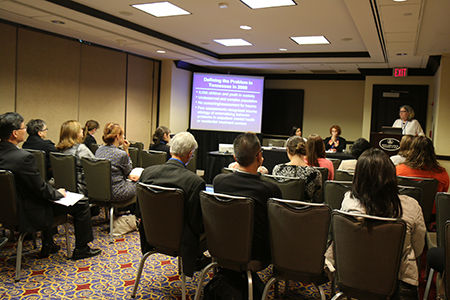 Image of 5 women sitting in front of a table presenting to group of individuals at a conference.