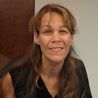 Headshot of Julie Petty, brunette woman smiling, on a dark background.
