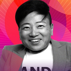 Image of a Korean-American woman with short hair wearing a blazer and a tshirt that says AND smiling at the camera.