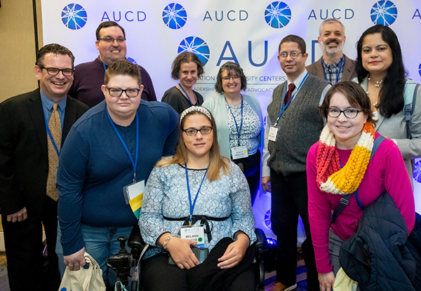 Image of 10 smiling individuals posing in front of the AUCD 2022 Conference banner.