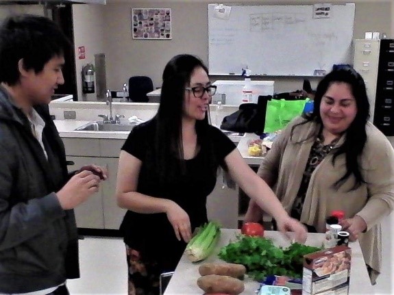 3 individuals standing at a table with vegetables. 