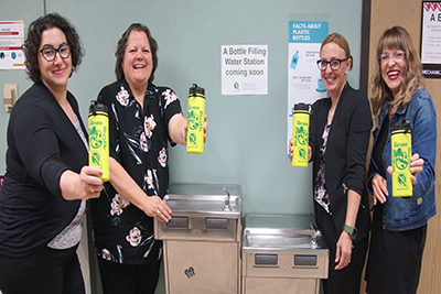 Image of four women holding water bottles standing next to the water fountain.