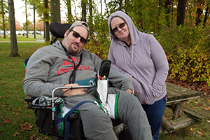 A man who uses a wheelchair in a park with his direct support professional.