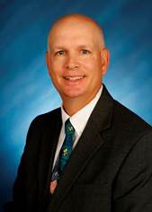Image of a bald white man wearing a suit and smiling at the camera.