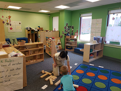 Image of a child and teacher building blocks on a classroom floor.