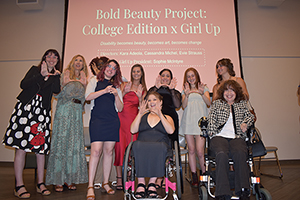 Image of a group of women standing on a stage with Bold Beauty Project: College Edition x Girl Up projected behind them.