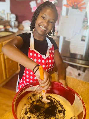 Image of a young black woman baking in a kitchen and smilng at the camera. 