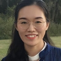 Headshot of a young asian woman with haired tied back wearing glasses and a blouse. 