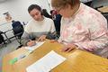 Isabelle Morris (left) writes with a pen while a writing student with a developmental disability looks on.
