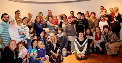 Group of individuals with RTS, their families, and UCCEDD staff, standing together in front of a wall for a group photo at an RTS event.