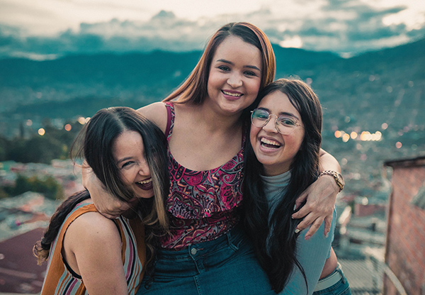 Image of three young women embracing and smiling at the camera.
