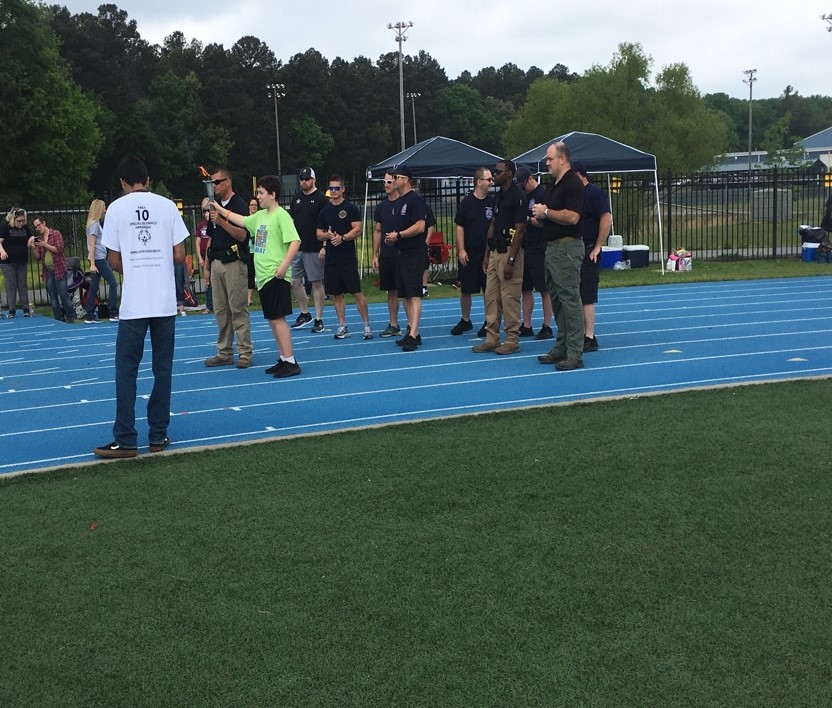 Students and Law Enforcement Officer holding Special Olympic Trophy on a track field.