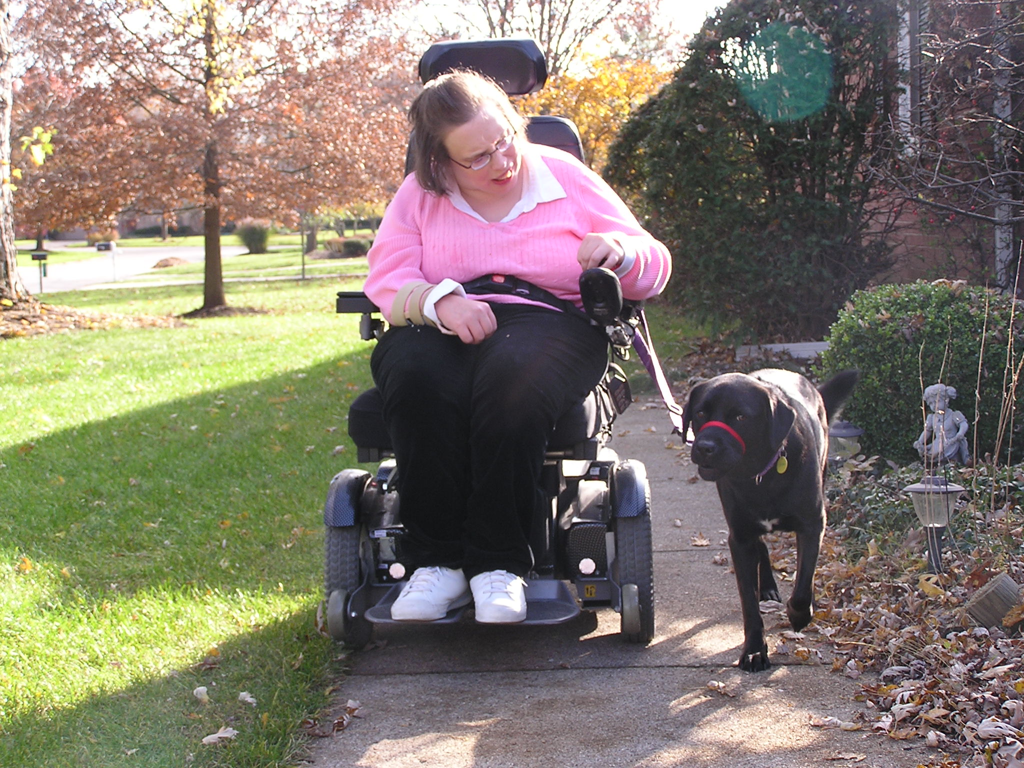 Susan using a motorized wheelchair with her service dog outside at a park.
