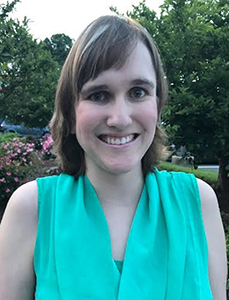 A young white woman with straight brown hair and wearing a green sleeveless shirt smiles for the camera.
