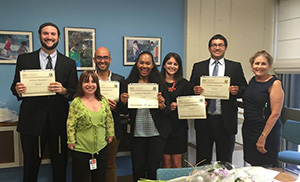 Photo of 7 people smiling for the camera, 5 of them holding completion certificates.