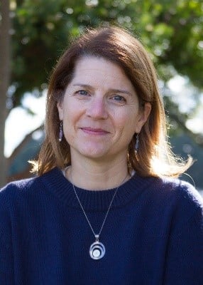 Photo of Aubyn Stahmer a smiling white woman standing outside wearing a blue sweater and silver necklace