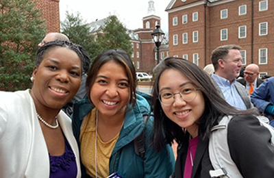 Image of three women wearing jackets standing outside with buildings in the background.