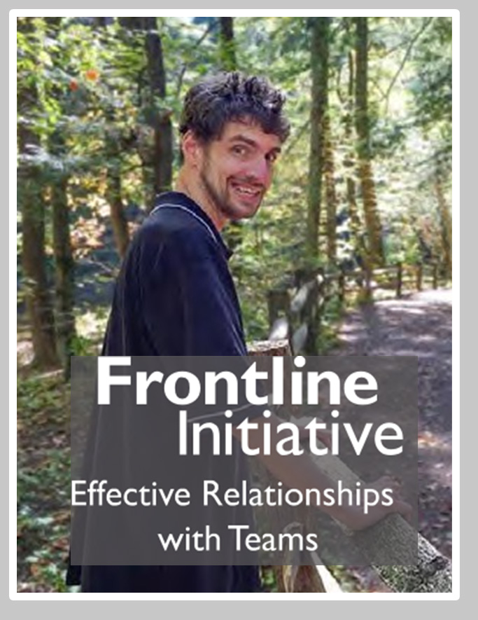Image of Nick Smith, a white man with a beard and dark hair wearing a polo shirt and jeans. He is standing in the woods.