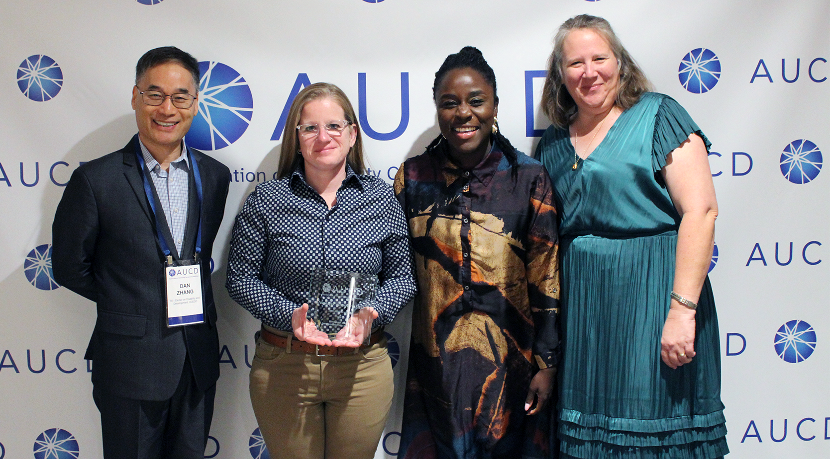 Awardee standing with colleagues in front of AUCD banner.