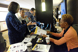Image of the NDSS booth with one Conference attendee speaking to two booth attendants.