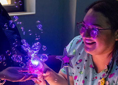 Image of UIHC Medical assistant Lizeth DeLeon, young woman with long brown hair wearing scrubs, uses sensory toy distractions to put patients at ease in the comfort room at the Center for Disabilities and Development.
