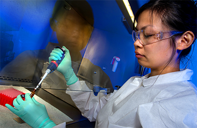 Young researcher wearing a lab coat and latex gloves performing an experiment at a laboratory.