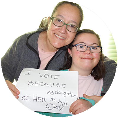 Image of mother and child sitting together and holding up a sign that reads "I vote because of my daughter mi higa"