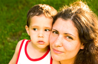 A mother and child cheek to cheek outdoors.