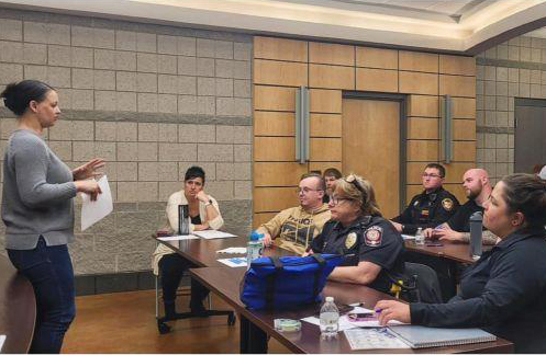A woman standing in front of a classroom presenting to a group law enforcment officers at the policy station.