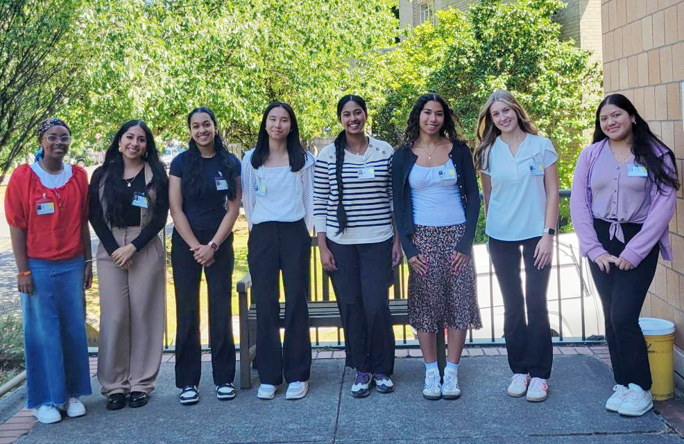 8 nicely dressed young adults are facing the camera, smiling, and lined up in a row on the shady patio of a brick building with greenery in the background Summary: This internship helped me grow not only as a student, but as a future provider and ally. I now carry a deeper understanding of how healthcare can empower or exclude, and a stronger commitment to making it truly inclusive for all. 