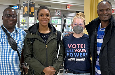  A group of four people (left to right): an African man, an African American woman, a white American woman, and an African man posing for a group photo at the airport, smiling into the camera. 