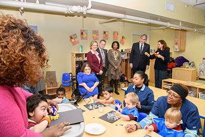 Image of classroom filled with children their care givers and adults looking on.