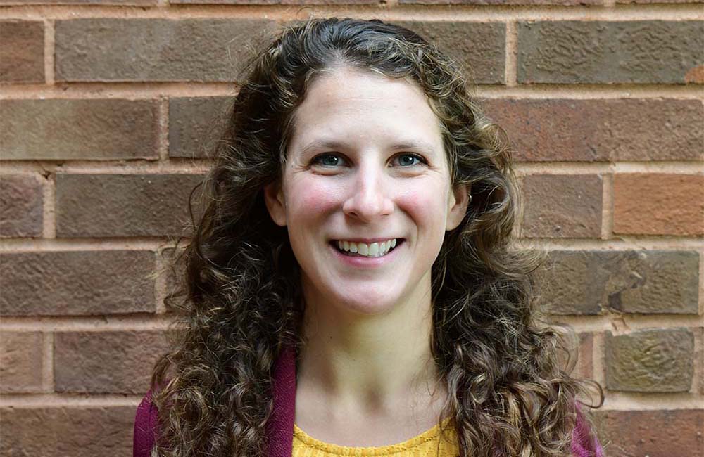  Image of Anna Bolgrien, a white woman with curly long brown hair, she is wearing a sweater and blouse. 