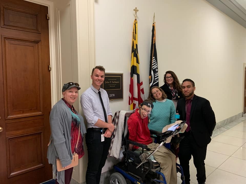  Six network members standing/siitting in front of an office door with the Maryland State Flag and the Flag of the US behind them.