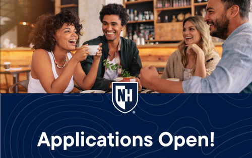 Four people sit around a table inside a café or bar setting with shelves of bottles in the background. Two people hold cups while others rest their hands on the table. A wide blue banner overlays the bottom of the image with a white NH shield logo and large white text reading “Applications Open!”