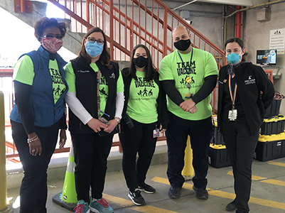 Image of five people masked wearing t-shirts and pants standing in parking lot with tote boxes behind them.