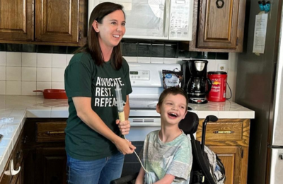 Mother administering food to their son in a wheelchair with feeding tube.