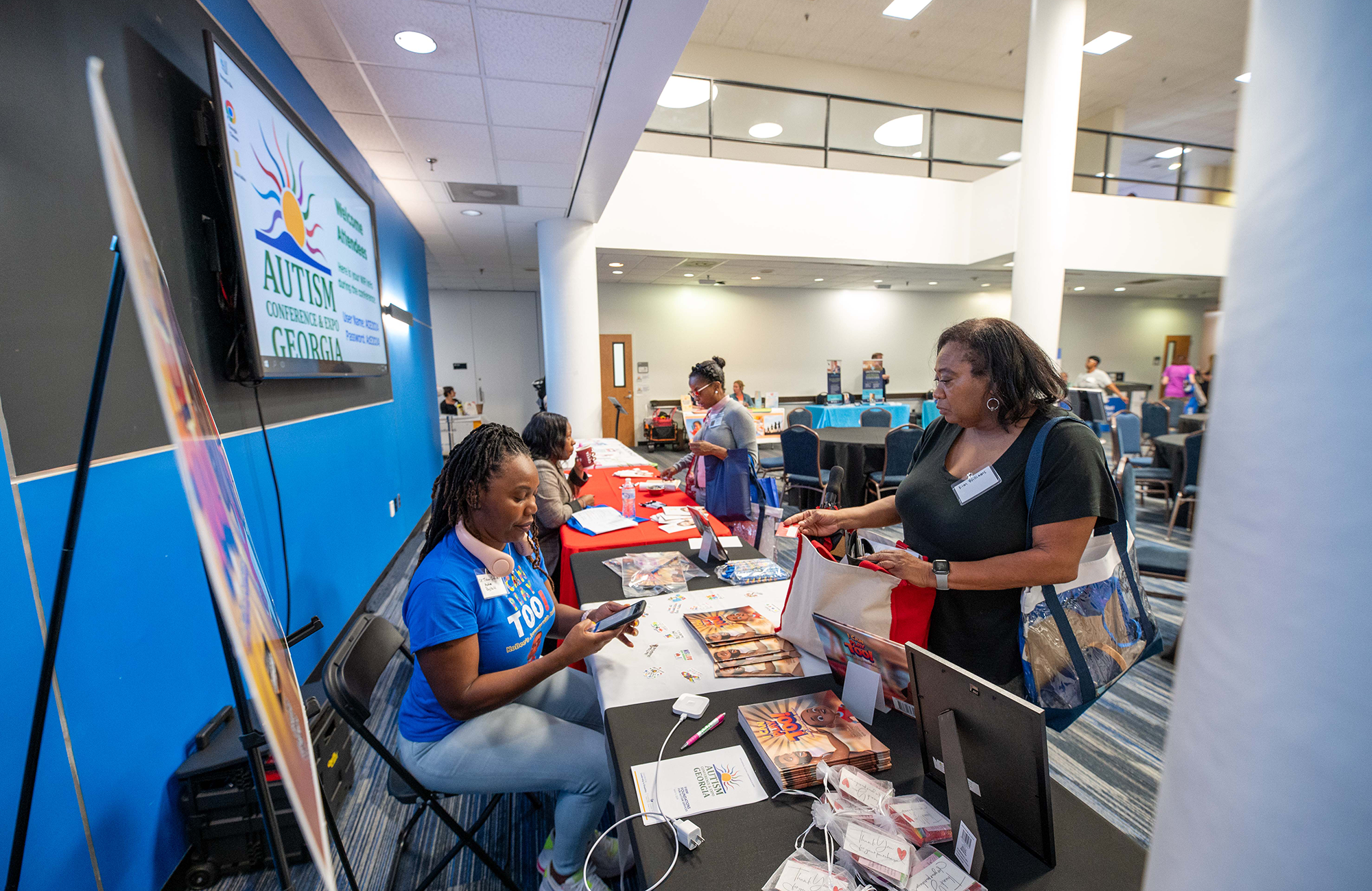  Black female attendee standing and talking to seated Black female exhibitor at autism conference.