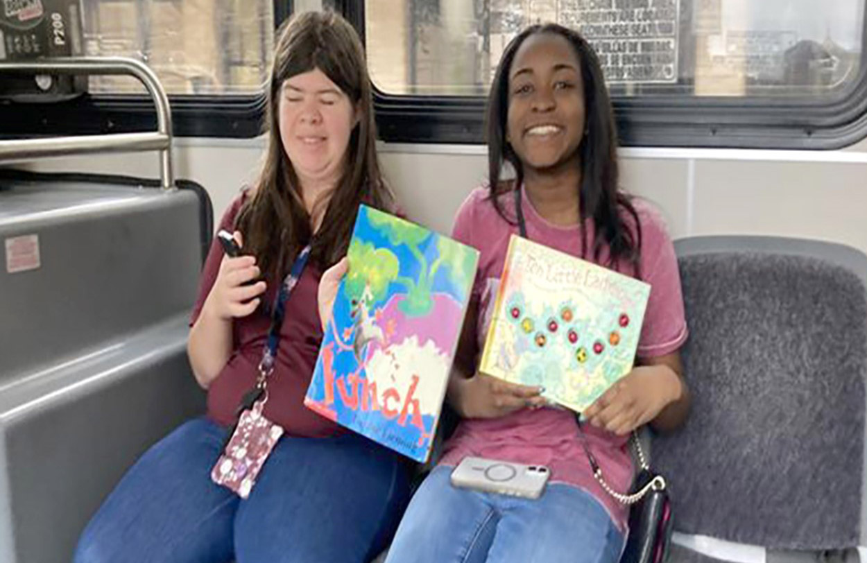 Two students holding books on a bus.