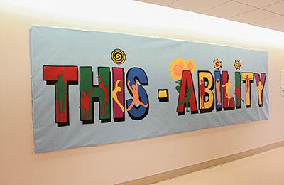  A large mural with the words "This-Ability" in multiple colors on a blue background. Within the letters are silhouettes of people in different poses. 