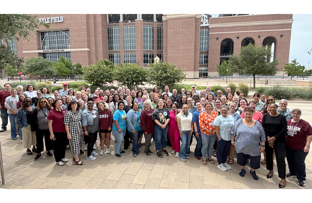 A large group of people stand in front of Kyle Field at Texas A&M University.