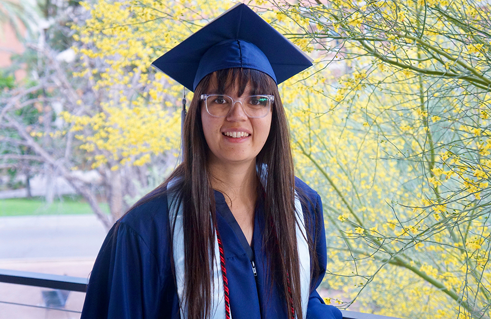Claire shown in graduation cap and gown with long brown hair and glasses